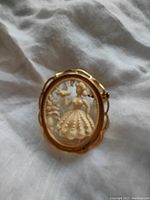 Front view of vintage brass brooch with carved celluloid lady and bird inside oval scalloped frame.
