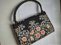 Front and side angle of vintage black handbag with floral embroidery in pastel colors.