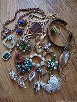 Full lot of vintage rhinestone jewelry and copper bracelet displayed on a wooden surface showing various rings, brooches, earrings, and a necklace with colored stones.