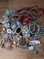 Overhead photo of various vintage costume jewelry pieces scattered on wooden surface including necklaces, brooches, earrings, bracelets