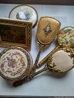 Overall view of 4 ornate vintage vanity items and framed artwork arranged together