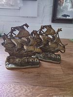 Pair of brass bookends shaped like vintage sailing ships shown on tabletop.