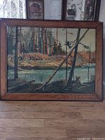 Full view of the framed vintage rustic Canadian wilderness painting on board showing forest and river landscape.