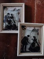 Front view of the two vintage silhouette glass framed pieces showing Victorian-themed black silhouette figures and decorative white frames.