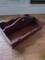 Front oblique view of vintage wooden utensil tray showing the two compartments separated by a central curved divider with a circular cutout handle and scalloped edges.