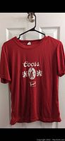 Front view of one red women's t-shirt featuring Coors Banquet logo in white centered on chest.