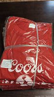 Photo showing bundled 10 red women's Coors Banquet T-shirts, sealed in plastic and wrapped with elastic bands.