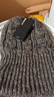 Front view of gray knitted winter hat showing texture and attached Dakine brand tag with price info.