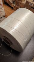 Side view of a large, tightly wound roll of white plastic twine with a shiny finish.