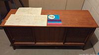 Wooden vintage stereo cabinet with speaker grills and documentation laid out on top.