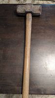 Photo showing the top side of the wooden sledge hammer with visible rust on the metal hammer head and a worn wooden handle.