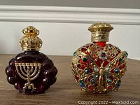 Pair of Czech glass perfume bottles on wooden surface, front view showing purple bottle with menorah and red bottle decorated with jeweled butterfly.