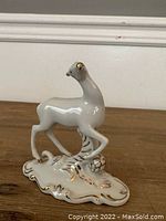 Porcelain white deer figurine with gold accents, standing on ornate base, showing front angled view.
