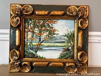Full front view of the framed oil on board painting showing the landscape scene with water, trees, and hills.