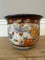 Full side view of the jardiniere showing colorful bird and flower motifs on a crackled glazed surface with a dark brown rim.