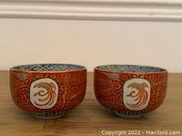 Front view of the pair of antique Japanese cups showing red exterior with gold phoenix designs inside white medallions.