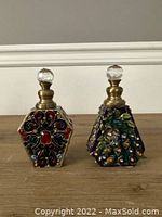 Pair of two Czech glass perfume bottles detailed with colorful enamels and stones, faceted glass stoppers on wooden surface.