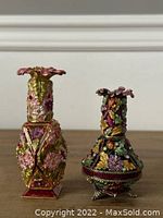Pair of two decorative perfume bottles with floral adornments on a neutral background.