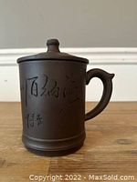 Front view of a dark brown Chinese Xisha clay tea mug with lid, showing engraved Chinese characters and solid handle.
