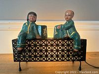 Side view showing the two ceramic Asian child figurines seated on the black metal lattice base of the lamp.