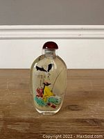 Front view of the Chinese reverse glass snuff bottle showing the painted figure in yellow fishing with a bird and calligraphy