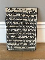 Rectangular art tile with musical notes printed in black on beige textured surface, front view resting on wooden surface against light wall