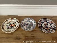 Three antique plates on wooden surface showcasing variety in shape, design, and size