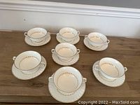Seven paired Royal Doulton soup bowls and saucers arranged on a wood surface, showing the overall lot contents.