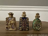 Three Czech glass perfume bottles with ornate filigree and colored rhinestones on a wood surface