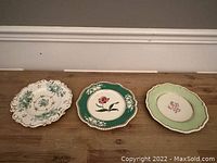 Three old English porcelain plates of different designs and colors placed on wooden surface, showing full view of plates