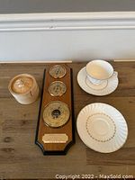 Photo showing the wooden mounted barometer with three dials, white teacup and saucer, and round wooden box with ship carving.