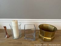 Wide shot showing four of the decorative items: clear glass hurricane candle holder with candle, clear square glass vase, brass octagonal planter, and small copper bud vase.