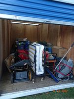 Interior view of storage unit showing rollaway cot, plastic totes, tool chest and bundled items