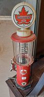 Full front view of the 18 inch tall red and white retro gas fuel pump showing steel base, plastic top, clear glass cylinder with measurement markings and red maple leaf Supertest globe on top.