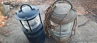 Two early heavy lanterns with glass globes and steel frames placed on the ground outdoors.