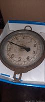 Antique circular hanging scale with aged dial and black pointer inside a brass frame.