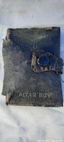 Worn black leather Bible case with visible wear and snap closure; shows front cover with 'ALTAR BOY' embossed text.