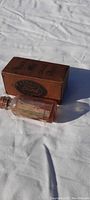 Photo showing antique Ford fuel gauge oil bottle and original factory Ford box outside on white cloth background.