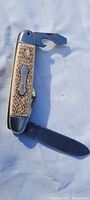 Antique pocket knife open showing blades and tool, bone-style textured handle with metal bolsters.