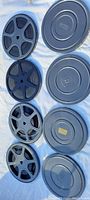 Four film reels placed next to four matching metal film canisters, showing condition and type of reels.