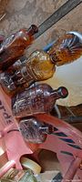 View of four bottles showing figural Native American bottle and three other embossed bottles on pink surface