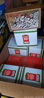 Stack of Coca-Cola North Pole Bottling Works collectible boxes, striped with red label and holiday wreath, showing multiple unopened boxes with two different polar bear skiing graphic designs