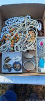 Box lot showing an assortment of pearl necklaces, colorful beaded necklaces, silver-tone jewelry with pendants, and various clip-on earrings.