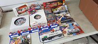 Overview of lot showing multiple boxed die-cast vehicles, racing transporter trucks, and collectible trading card packs arranged on floor with driver imagery on boxes.