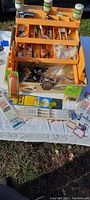 Overall photo of the open orange tackle box showing compartments with assorted fishing lures, small bottles of bait, packaged hooks, and other fishing accessories.