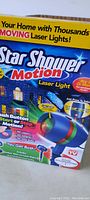 Photo showing the original sealed packaging of Star Shower Motion Laser Light with colorful graphics, including product image and key features.