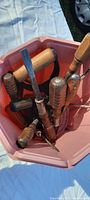 Top-down view of various heavy handled screwdrivers with wooden and metal handles, placed inside a pink plastic bucket.