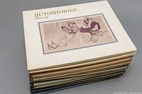 Top view of the stack of 10 automobile quarterly hardcover books showing the white cover of the top volume with vintage car illustration.