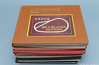 Stack of 11 hardcover volumes, various colors with 'Automobile Quarterly' title visible. Top journal cover titled 'Brooklands 1907-1939' with a racing track design.