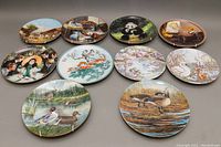 Twelve porcelain collectible wall plates arranged in a three-by-four pattern, showing various wildlife, indoor, and group figure designs.